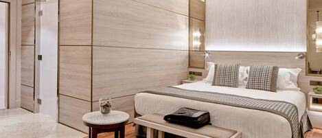 Una habitación de hotel moderna con una cama grande, una mesita de noche, un banco y una pequeña mesa redonda.