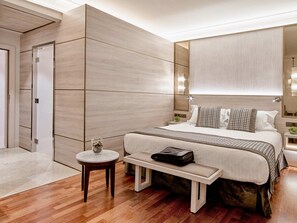 A modern hotel room with a large bed, a bedside table, a bench, and a small round table.