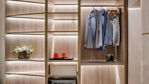 A modern, multi-tiered storage unit with shelves and hanging space, a small refrigerator, and a vase with flowers. - Hotel Preciados (Madrid)