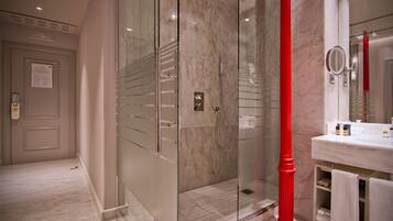 Un baño moderno con cabina de ducha de vidrio, suelo de baldosas de mármol y tocador blanco con un detalle en color rojo.