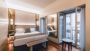 A modern hotel room with a large bed, bedside tables, a bench, a small table, and a balcony with a railing. - Hotel Preciados (Madrid)