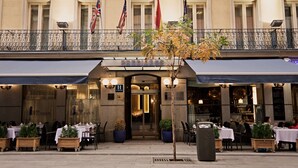 A hotel entrance with outdoor seating, flags, and a sign reading "Hotel Preciados". - Hotel Preciados (Madrid)
