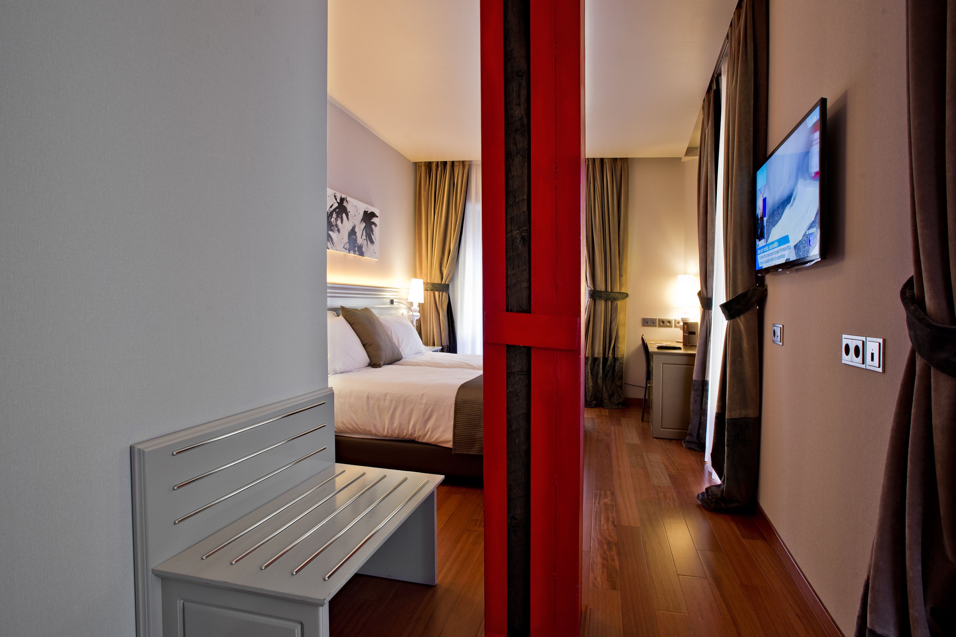 A hotel room with a bed, a bench, a TV, and a bathroom.