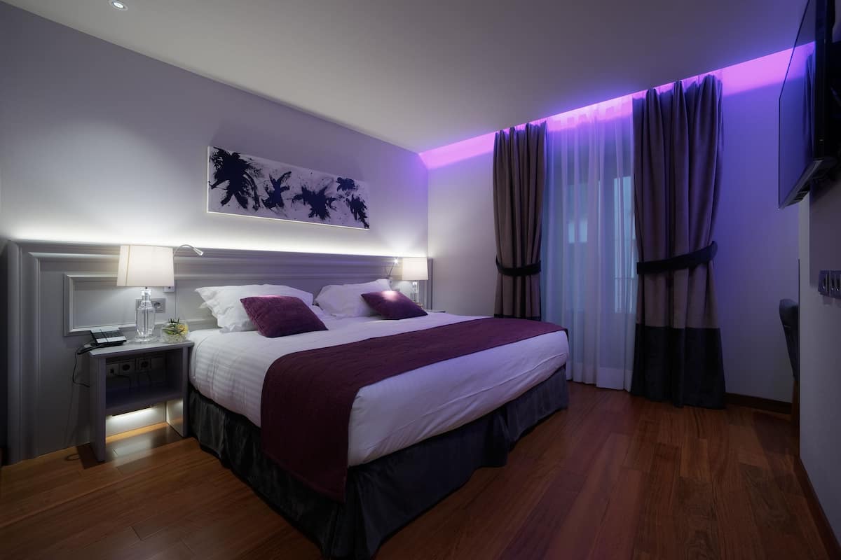 A modern bedroom with a large bed, bedside lamps, a nightstand, a wall-mounted artwork, and a ceiling light.