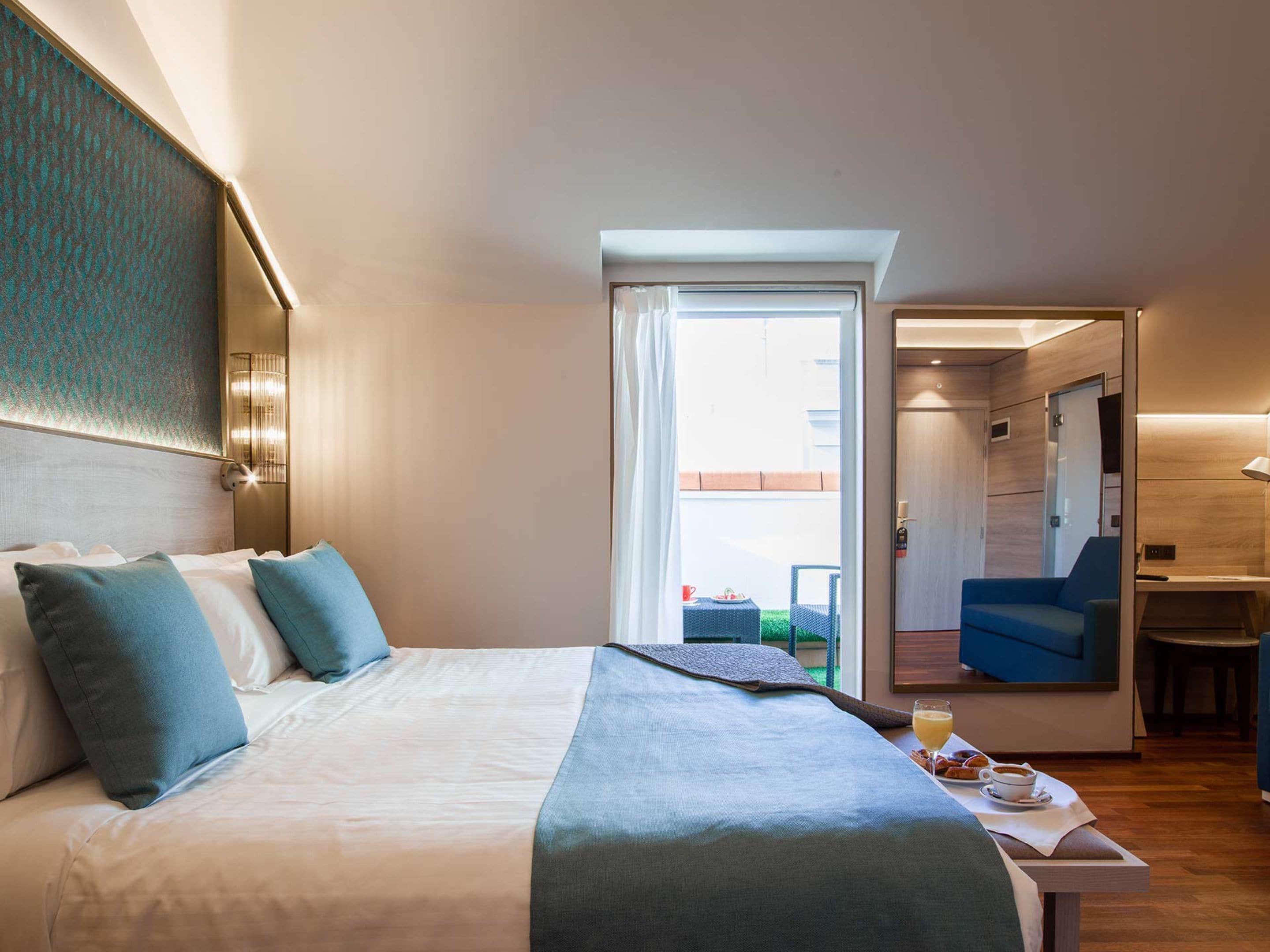 A hotel room with a bed, a desk, and a chair. There is a window with a view of the outside.
