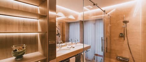 Un bagno moderno con un mobile vanitario in legno, cabina doccia in vetro e una mensola a incasso con una ciotola di frutta.