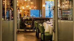 A restaurant interior with a bar area, green upholstered chairs, and hanging spherical light fixtures. - Hotel Preciados (Madrid)