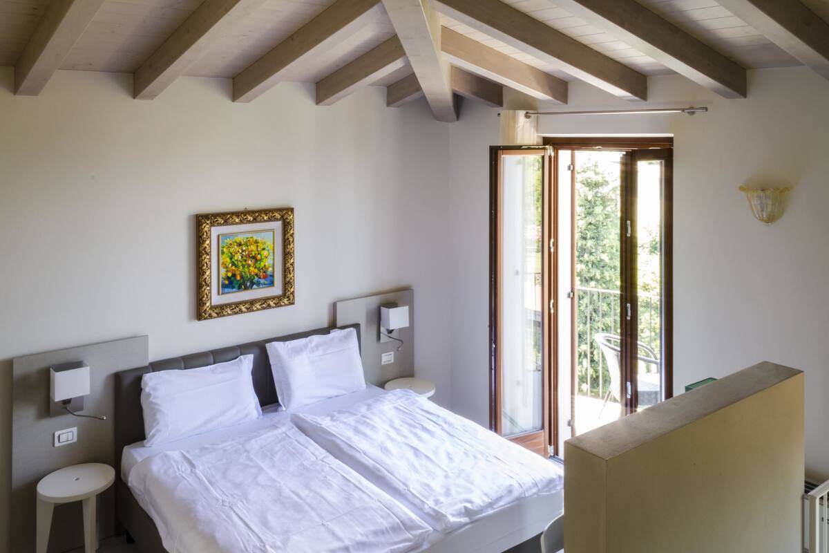 A bedroom with a bed, bedside tables, a painting, and a sliding glass door to a balcony.