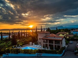 A resort with a swimming pool, lounge chairs, and a view of the sunset over a lake. - Relais agli Olivi (Lazise)