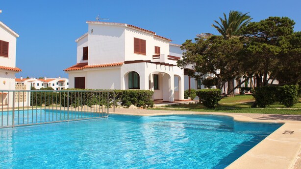Una piscina con agua cristalina azul, rodeada de edificios blancos con techos rojos y una palmera.