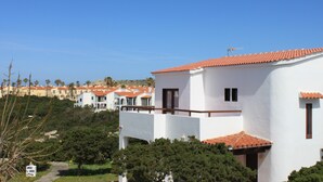 Un edificio blanco con techo de tejas rojas, rodeado de follaje y otros edificios parecidos al fondo.