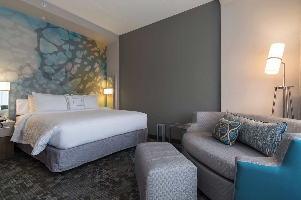 Quarto de hotel com cama, sofá, uma mesinha e abajur.