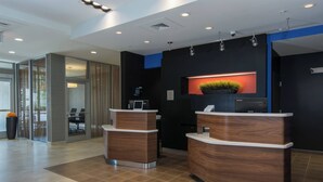 A reception area with two wooden reception desks, a potted plant, and a computer on the wall. - Courtyard Raleigh-Durham Airport/Brier Creek (Raleigh)
