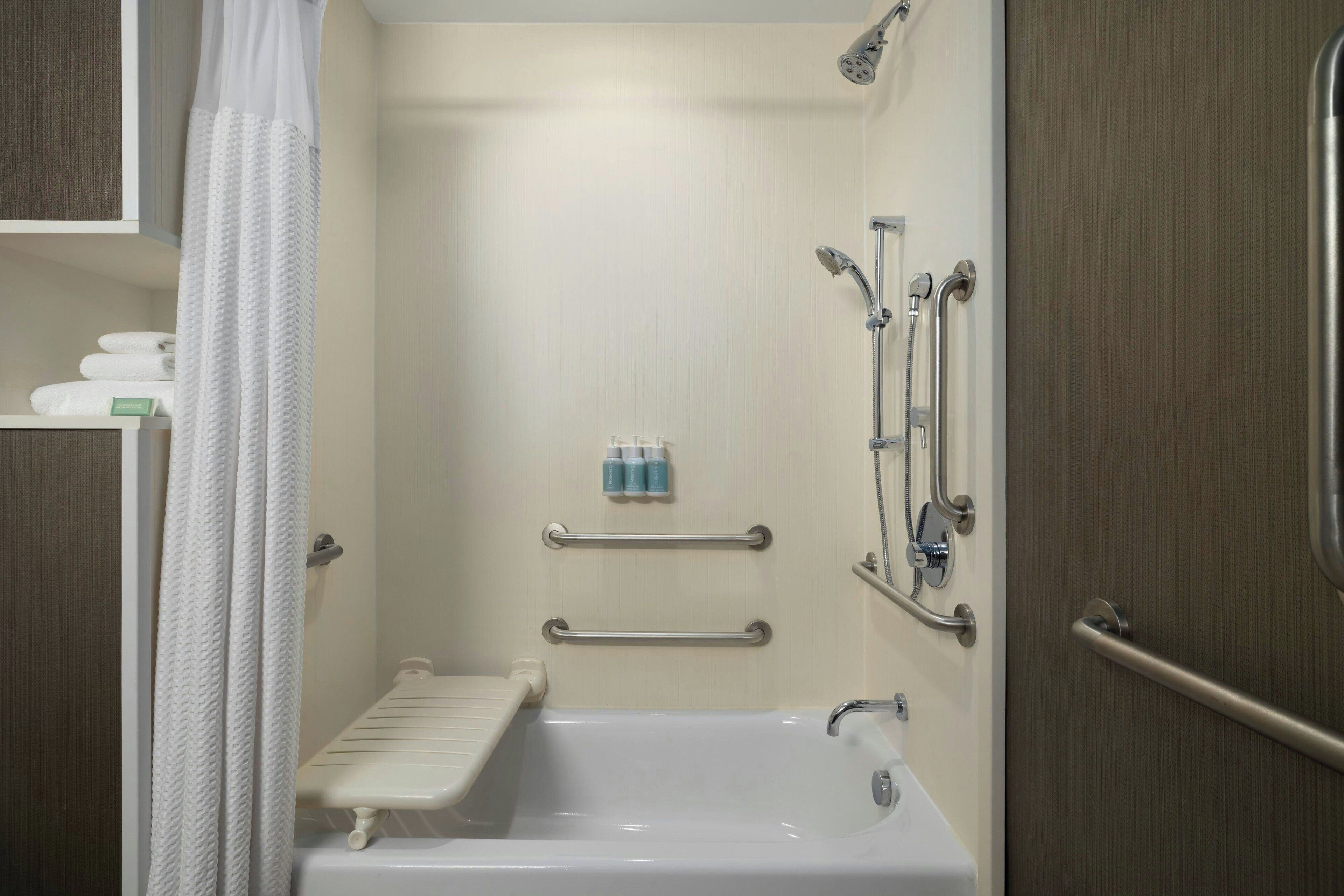 A standard bathroom with a bathtub, a shower, and a toilet. There are grab bars installed for safety.