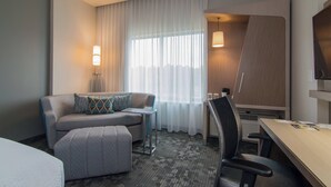 A hotel room with a sofa, a small table, a desk, a chair, a TV, and a window with curtains. - Courtyard Raleigh-Durham Airport/Brier Creek (Raleigh)