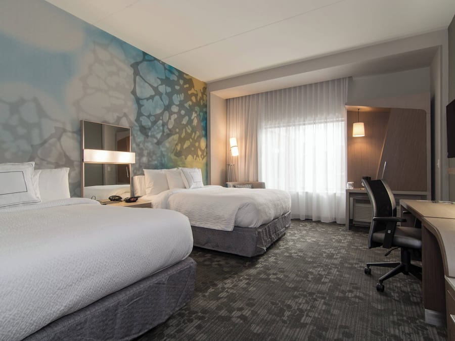 A hotel room with two beds, a desk, a chair, a TV, and a bathroom.