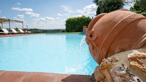 A pool with a terracotta water feature, surrounded by lounge chairs and a clear sky. - Il Palazzetto (Siena)