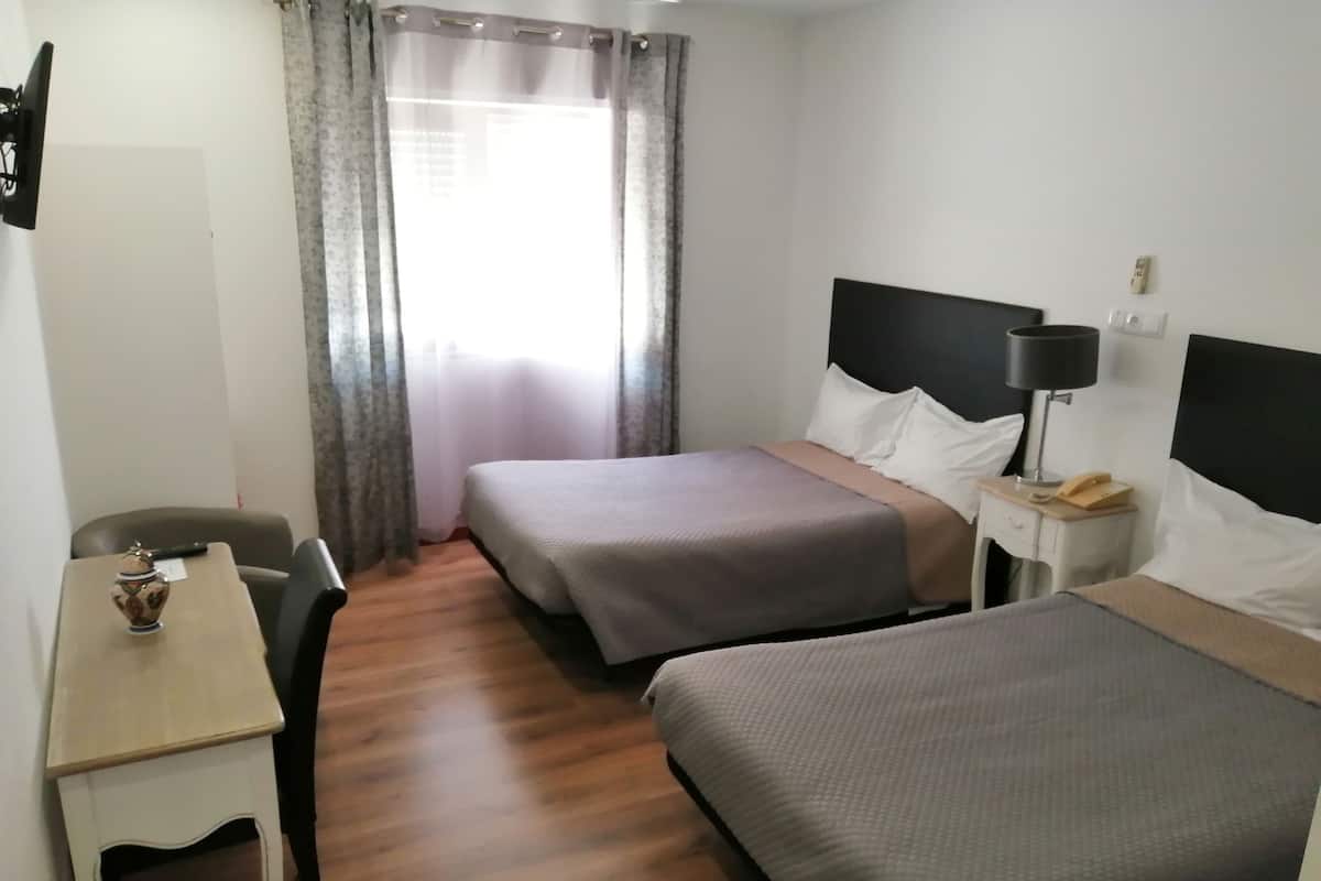 Habitación de hotel con dos camas individuales, un escritorio pequeño con una silla, una lámpara y un ventanal con cortinas.