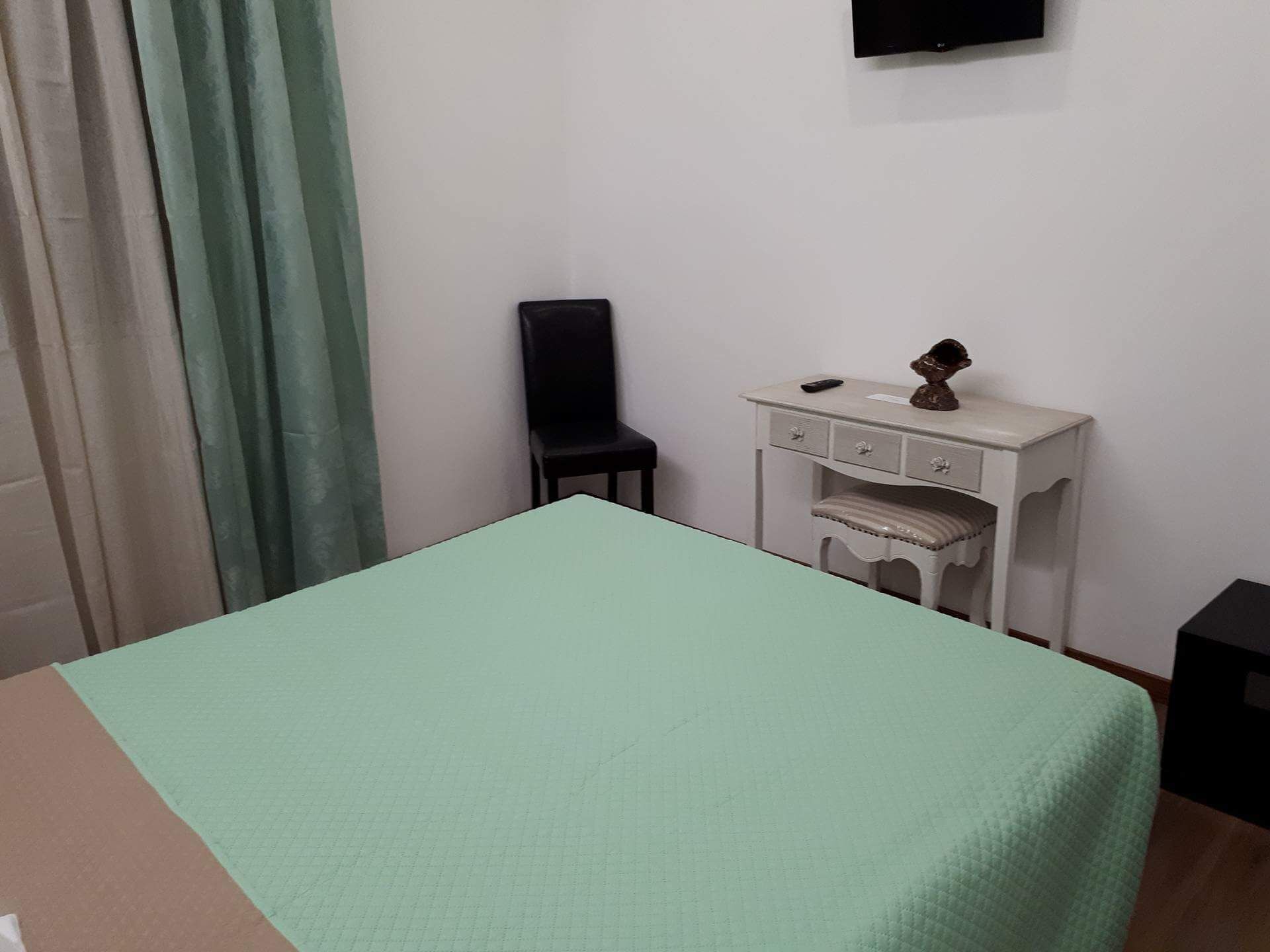 Une chambre comprenant un lit, un petit bureau avec des tiroirs, une chaise et un téléviseur fixé au mur.
