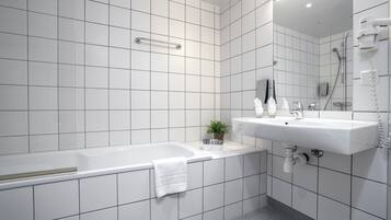 Un baño moderno con baldosas blancas, una bañera, un lavabo, un espejo y un cabezal de ducha de mano.