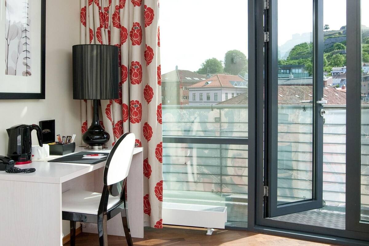 Ein Zimmer mit Schreibtisch, Stuhl, Lampe und Blick auf Gebäude durch eine Glastür.