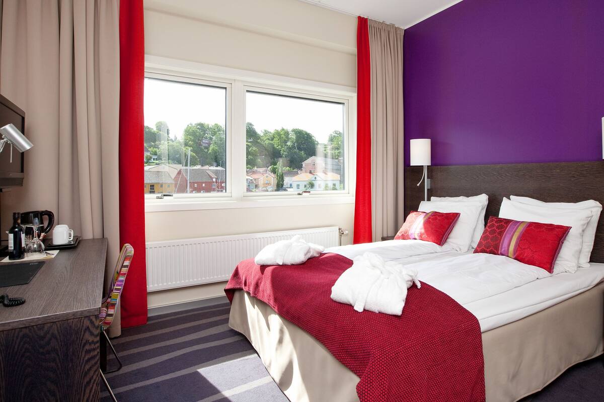 Ein Hotelzimmer mit einem Bett, einem Schreibtisch, einer Lampe und einem Fenster mit Vorhängen.