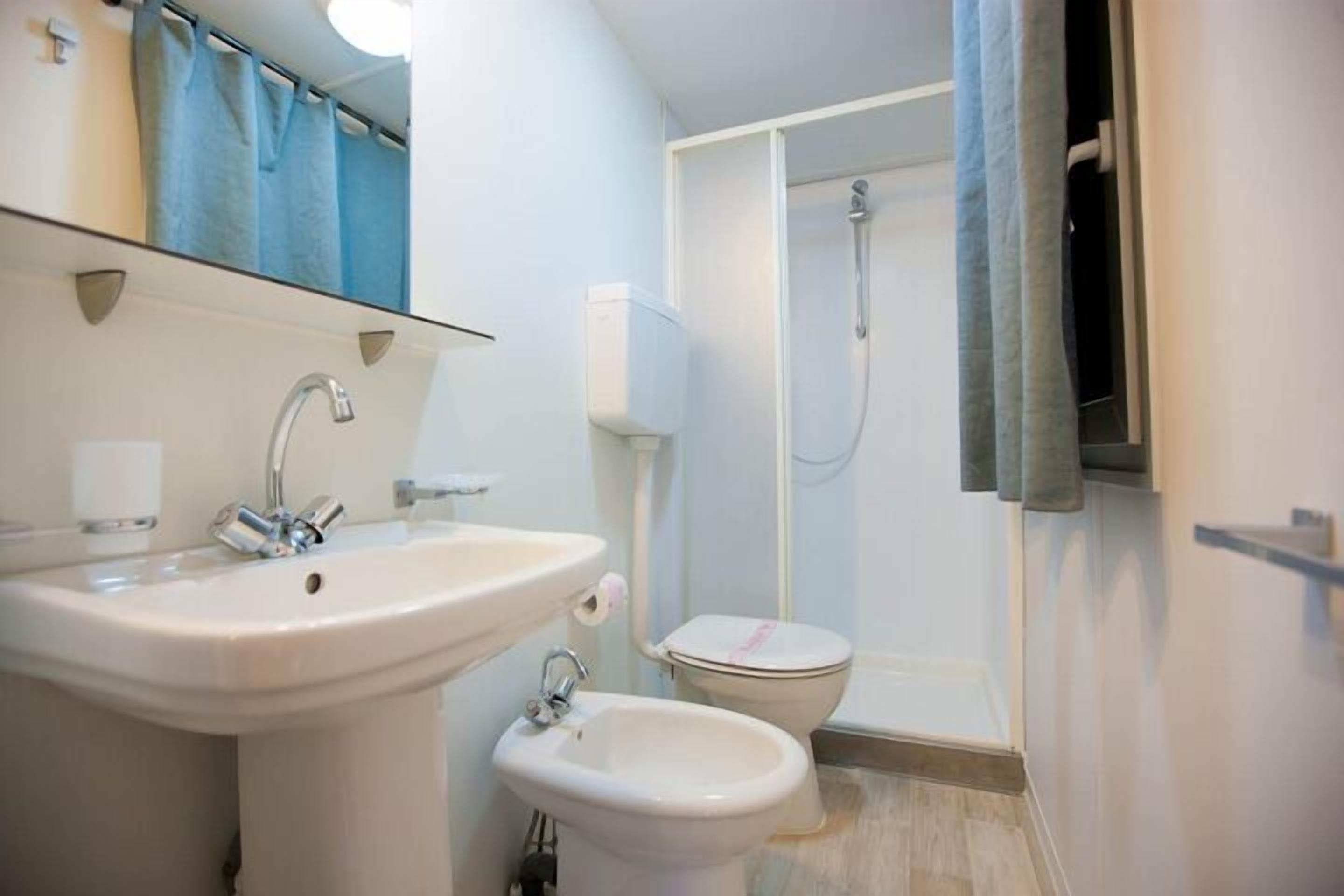 Et badeværelse med vask, bidet, toilet og bruser.