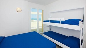 Habitación con literas, puerta corrediza al balcón y lámpara fijada a la pared.