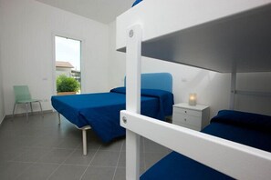 A room with bunk beds, a bedside table with a lamp, a chair, and a window with a view of greenery. - Villaggio Camping Blu (Senigallia)