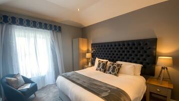 A bedroom with a large bed, a chair, a bedside table, and a lamp.