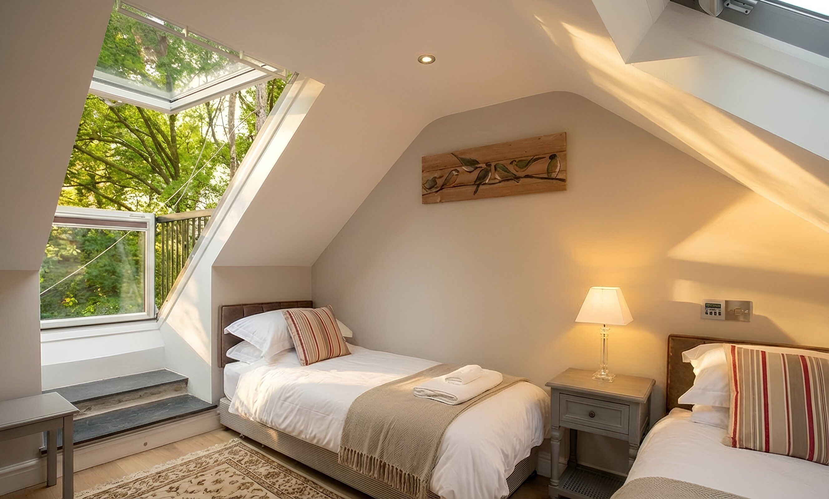 A bedroom with a skylight, a bed, bedside tables, a lamp, and a painting on the wall.