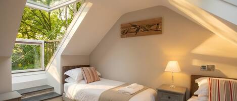 A bedroom with a skylight, a bed, bedside tables, a lamp, and a painting on the wall.