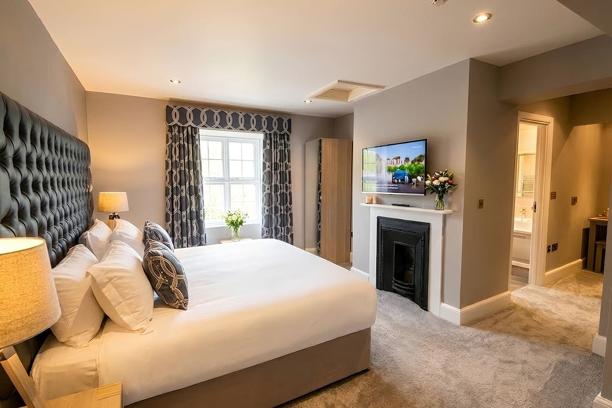 A modern hotel room with a large bed, a fireplace, a television, and a view of the outdoors.
