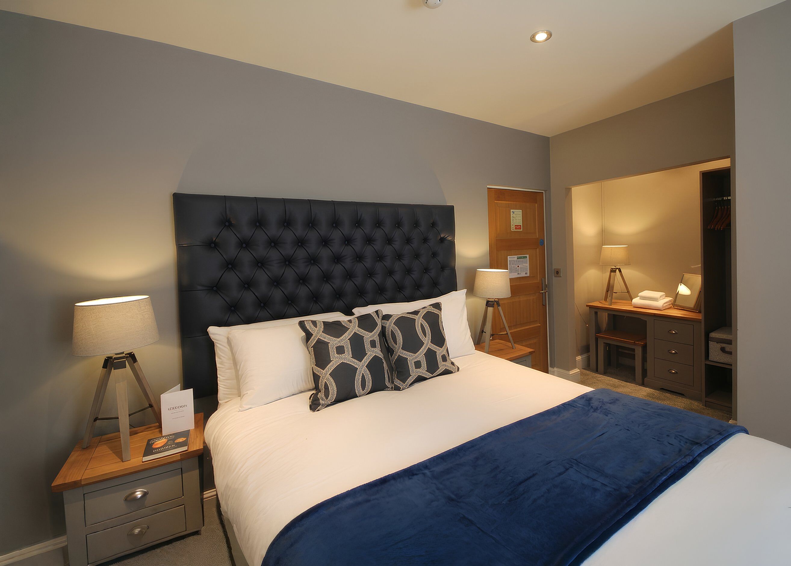 A bedroom with a tufted headboard, a bed with white linens, two bedside tables with lamps, and a wooden nightstand with drawers.