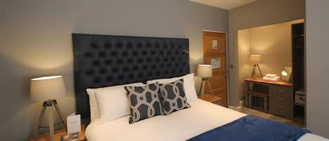 A bedroom with a tufted headboard, a bed with white linens, two bedside tables with lamps, and a wooden nightstand with drawers.