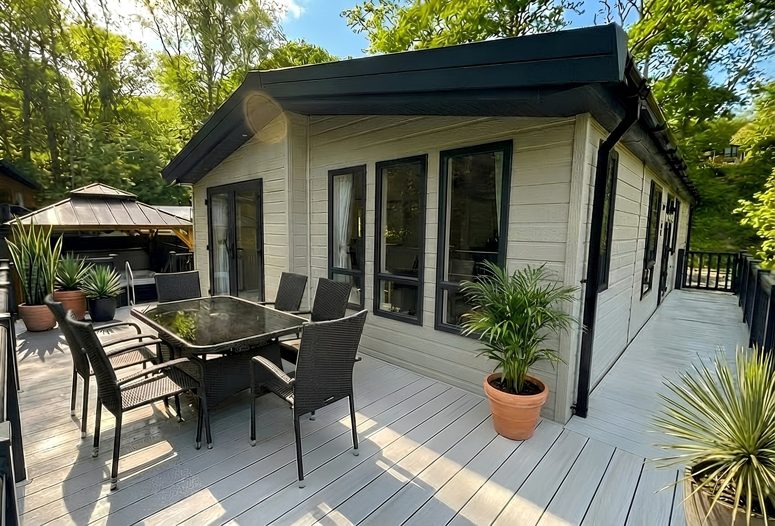 A house with a deck, a dining table with chairs, and potted plants.