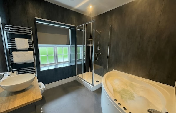 A modern bathroom with a bathtub, shower, and a window. - Aberdunant Hall (Porthmadog)