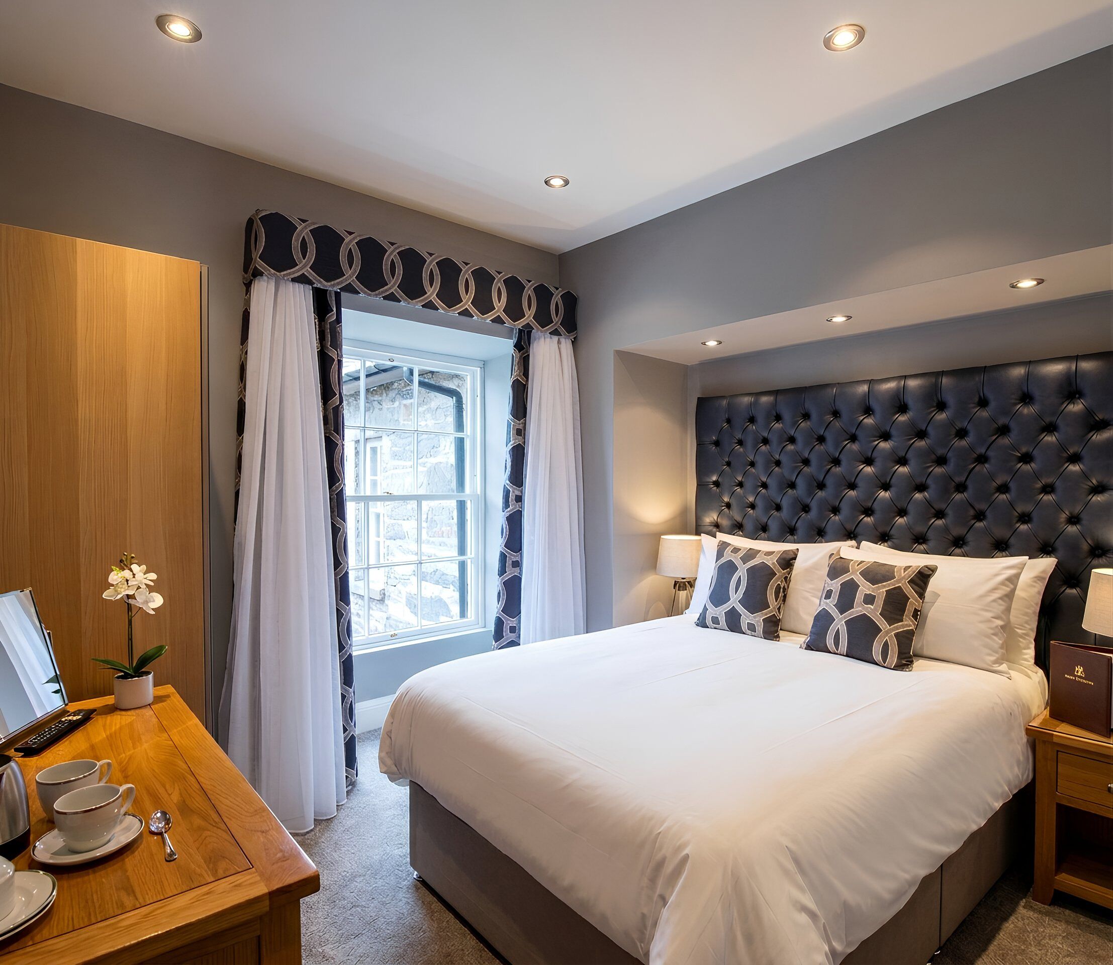 Ein Hotelzimmer mit einem großen Bett, einem Holztisch mit einem Computer und einem Fenster mit Vorhängen.