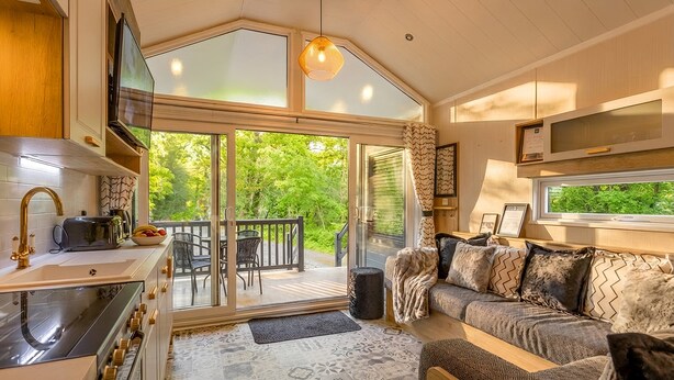 A cozy cabin interior with a kitchen, dining area, and a sofa with patterned cushions. - Aberdunant Hall (Porthmadog)