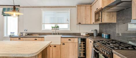 A modern kitchen with wooden cabinets, a built-in dishwasher, a stove, and a window with blinds.