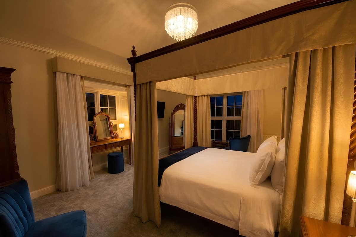 A four-poster bed with curtains, a chandelier, and a mirror in a hotel room.
