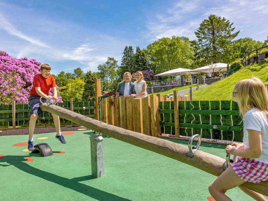 A playground with seesaws, a green surface, and a wooden fence.