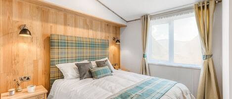 A bedroom with a wooden headboard, a bed with a plaid blanket, bedside lamps, and a nightstand with a lamp.
