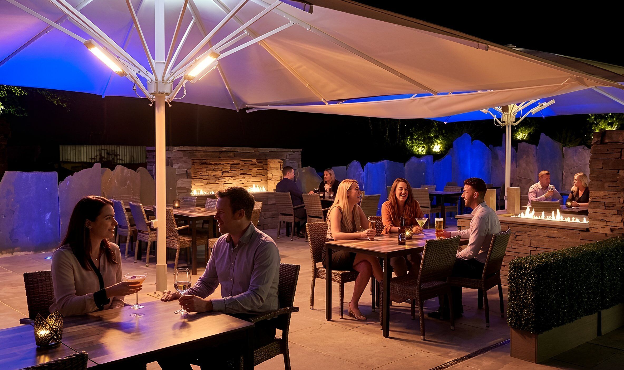 An outdoor dining area with tables and chairs, a stone wall, and a fire feature.