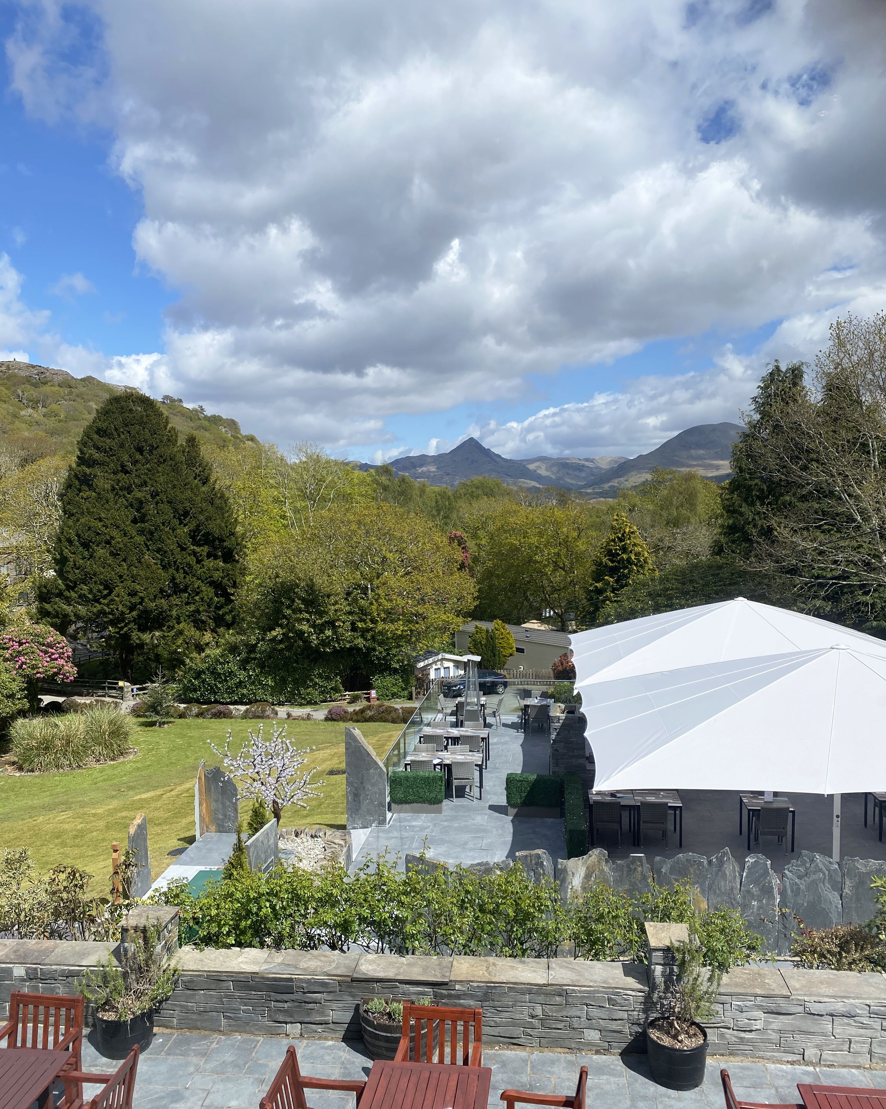 Un patio con mobiliario exterior, una sombrilla blanca y vistas a una cadena montañosa.