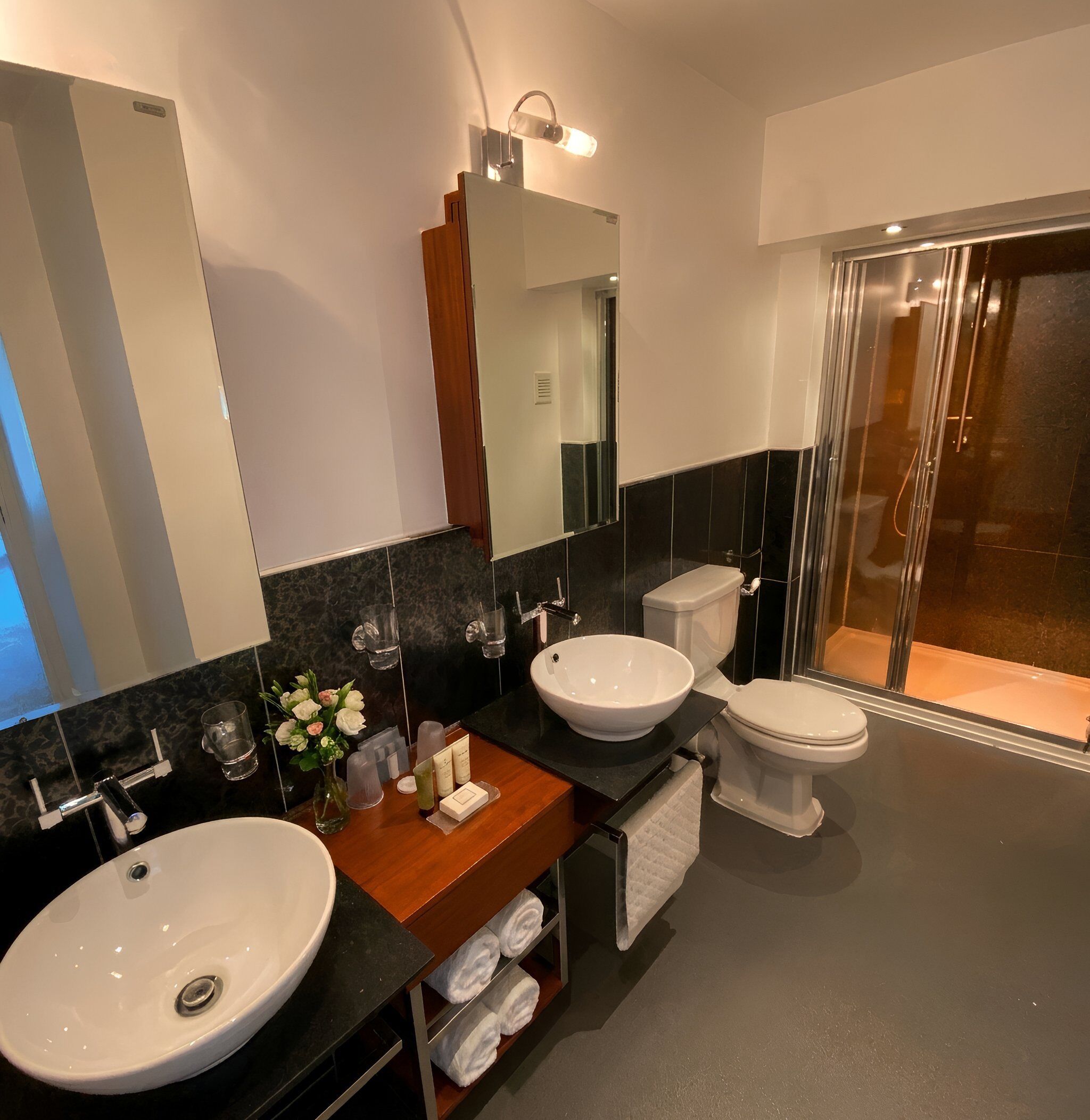 A modern bathroom with two sinks, a toilet, a shower, and a large mirror.