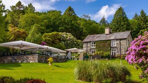 A stone building with a garden, a covered outdoor seating area, and a view of the surrounding greenery. - Aberdunant Hall (Porthmadog)