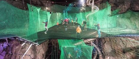 A large indoor space with multiple levels connected by walkways, featuring netted climbing areas and various structural elements.