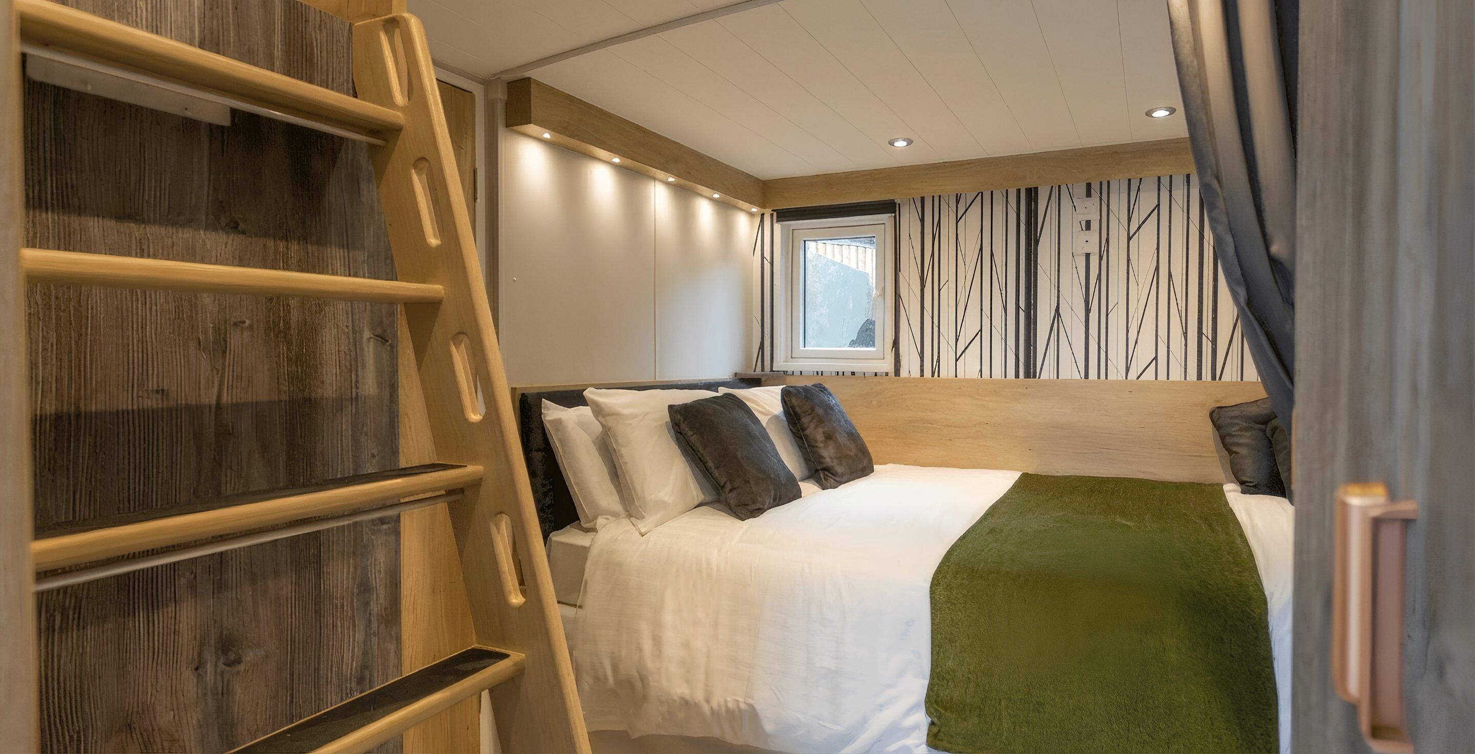 Un dormitorio con una cama, un edredón verde, una escalera de madera y una ventana con vistas.