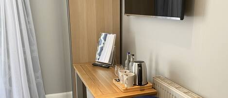 A room with a blue armchair, a wooden desk with a picture frame, a kettle, and two mugs.